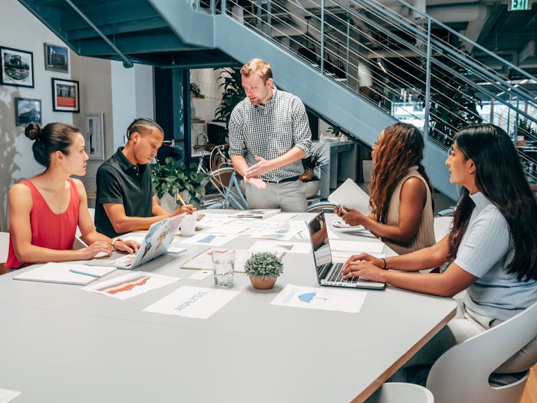 A diverse group of colleagues collaborating on a project in a modern office setting with laptops and documents.