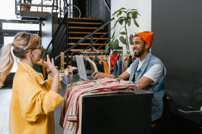 A customer and clerk engaging in conversation at a fashionable clothing store counter.