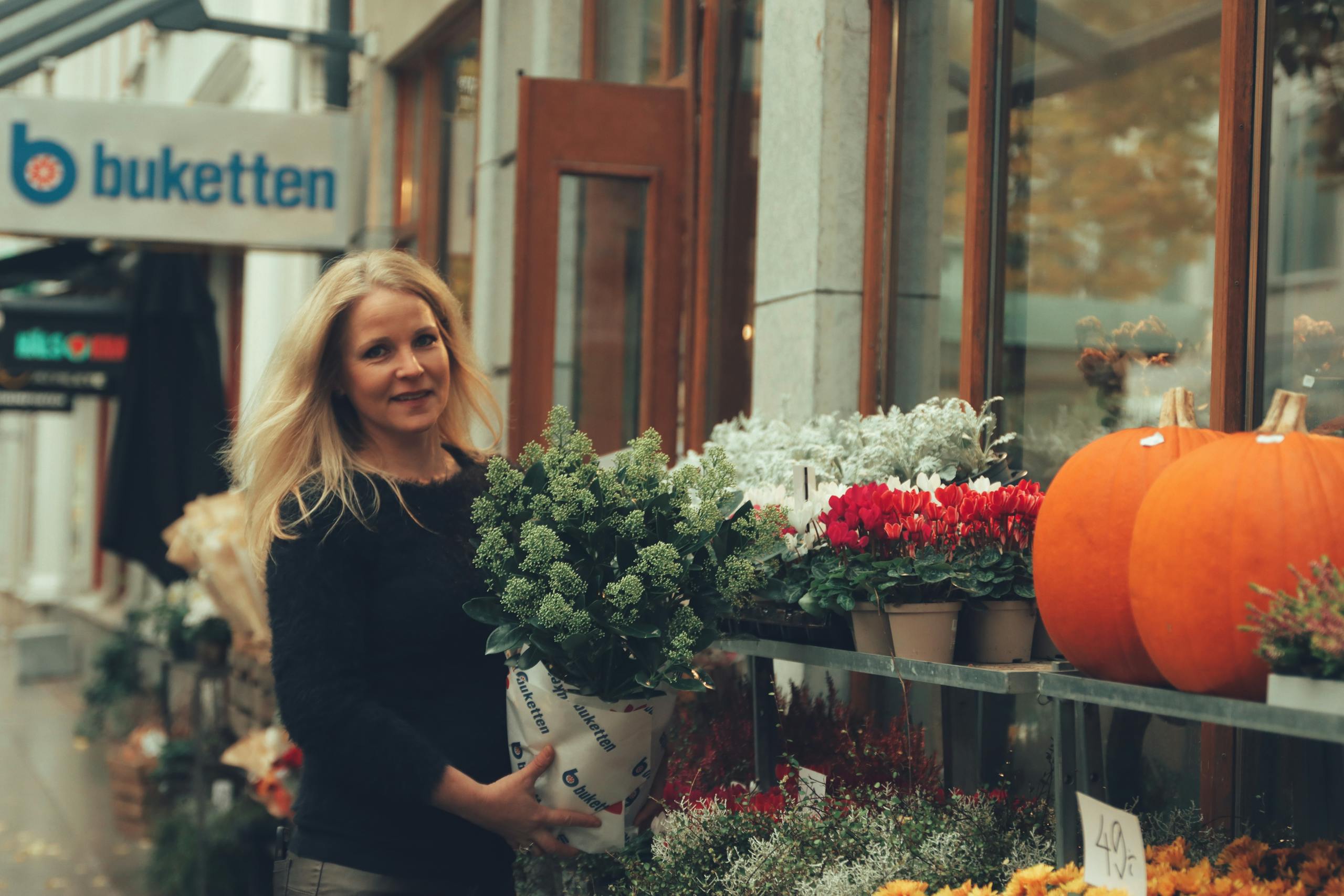 A woman outside a floral shop in Jönköping, Sweden, holding a potted plant.