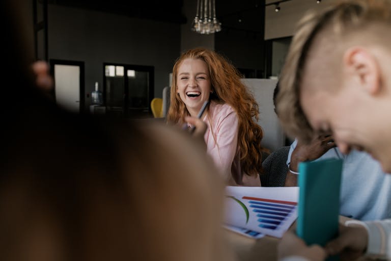 Joyful red-haired woman laughing during a casual meeting indoors.