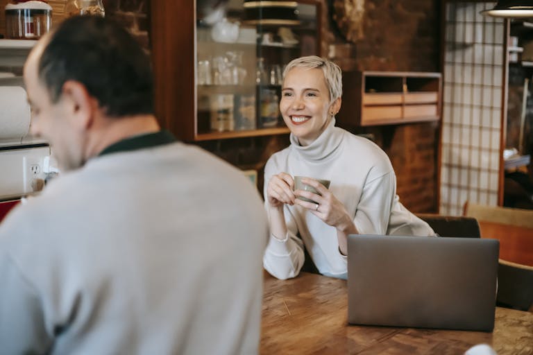 A cheerful couple having coffee and conversation in a cozy indoor setting, with a laptop on the table.