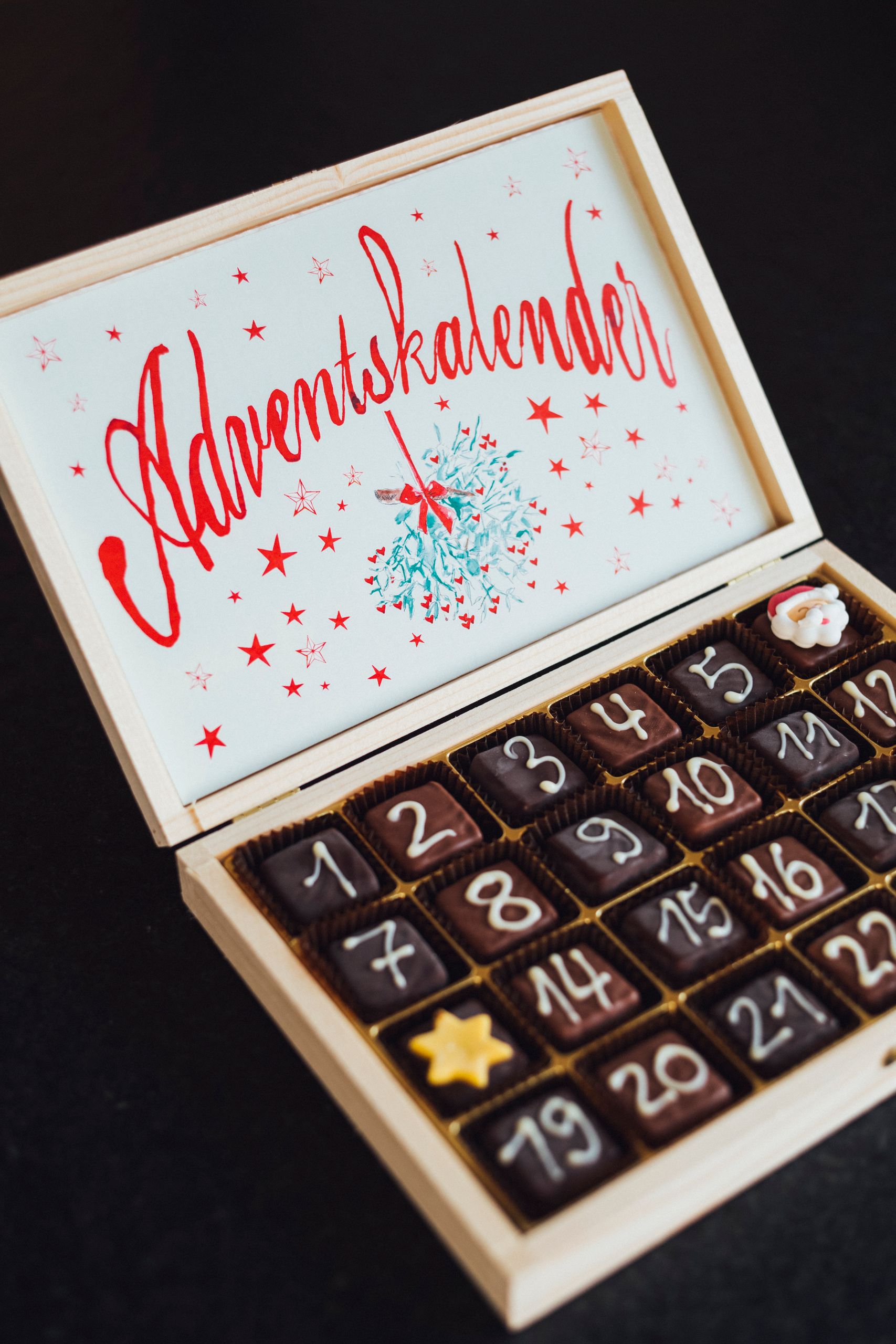 Wooden advent calendar filled with chocolates, decorated with numbers and stars.