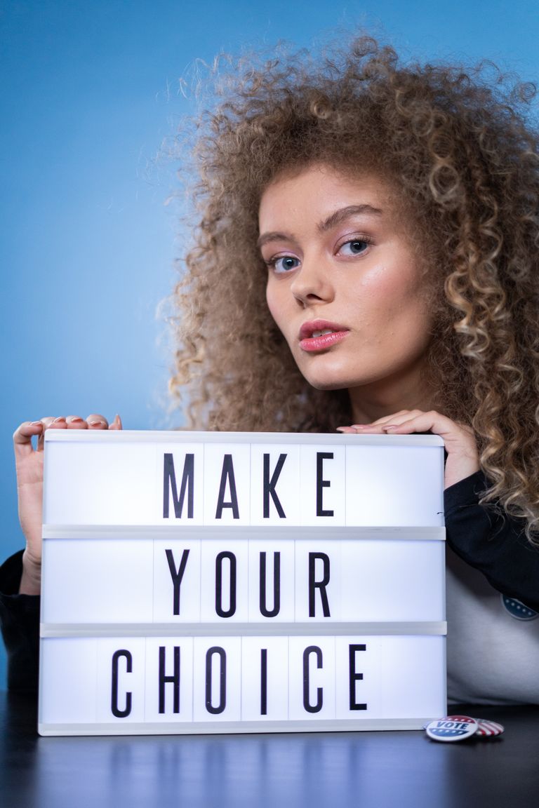 Young woman with curly hair holding a motivational sign with the message 'MAKE YOUR CHOICE'.